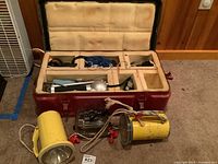 Overall lot contents showing heavy metal case with foam padding open and scuba diving gear, underwater lights, and clear camera housing displayed outside.