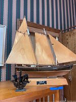Wooden schooner model with two tan sails on wooden base with metal nameplate 'Schooner 1901 America' and small metal Nina model in front, side view