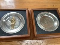 Two framed wall plates side by side: 12x12 wood frames with black mats, each containing 8" diameter silver and gold plated Easter plates