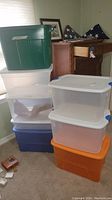 Stacked plastic storage bins of various colors and sizes in a room corner.