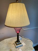 Front view of vintage table lamp showing pink and clear swirled glass body and pleated beige shade, sitting on a marble base.