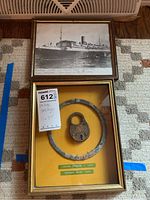 Framed photo of the Mohawk cruise ship with handwritten notation of sinking date and cause alongside framed salvage relics: locker opener ring and padlock.