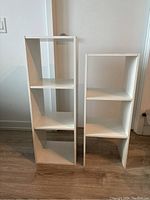 Front view of two white wooden stands with three open shelves each, one taller than the other.