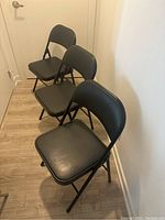 Side angle view showing three black foldable chairs with padded seat and backrest arranged in a row.