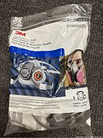 Front packaging of 3M small half-face respirator showing sealed bag with respirator visible inside, product name and usage images on bag.