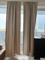 Pair of beige blackout curtains hanging in front of glass door with balcony view.
