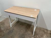 Front and side angle showing the wood-top desk with two white drawers and white legs.