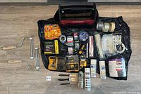 Full overview of construction supplies laid out on black tool bag including paint, brushes, fasteners, tools, and tapes