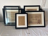 Seven black photo frames arranged on a flat surface with 'DOCUMENT DOCUMENTO' placeholder papers inside most frames.