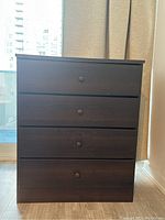 Front view of dark brown wooden dresser with four drawers and round knobs.