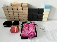 Large assortment of stacked jewelry boxes in various colors with velvet pouches on a white table against a white wall.
