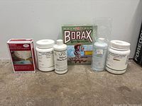 Photo showing six bottles and boxes of jewelry making chemicals and supplies including Borax, Silver Blackener, Resin, and powders on a gray surface.