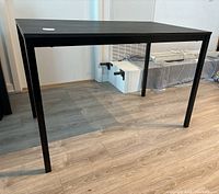 Black rectangular kitchen or dining table shown from an angle under bright indoor lighting.