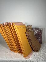 View of 25 yellow Uline bubble mailers, 12 brown kraft paper bags, and wrapped packing paper bundle.