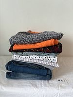 Stack of folded men's clothing including shirts, t-shirts, shorts, and jeans in various patterns and colors.
