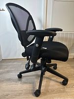 Side-angle image showing black mesh backrest, padded seat, adjustable armrests, and caster base.