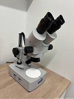Omax binocular stereo microscope with dual eyepieces, zoom knobs, illuminated stage on wooden surface