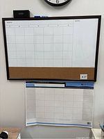 Dry erase weekly planner framed on wall with marker and eraser on top, cork strip at bottom, blank grid layout for days and notes section