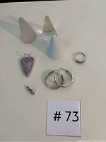 All jewelry items and ring holders visible in the lot, including one silver ring, two silver hoop earrings, two pendants (one heart-shaped amethyst, one with cubic zirconia), and three ring holders made from different materials.