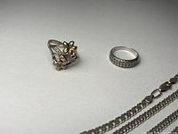 Photo showing two rings placed side by side and part of a chain necklace section visible on white background.