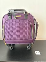 Front view of purple Aimee Kestenberg carry-on bag with quilted front panel and dual handles, showing detail of wheels and handle attachments.
