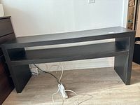 Front view of black wood TV stand showing top surface and open lower shelf.