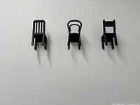 Set of 3 black mini chair wall hanger hooks mounted on a white wall, showing front and top views.