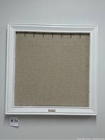 Full view of white wooden frame with beige fabric backing and hooks at top for jewelry hanging.