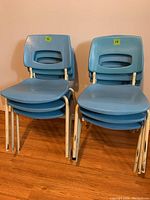 Two stacks of blue plastic school chairs with white metal legs against a wall.
