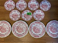 Top view showing eight dishes in first set with red pastoral landscape pattern, four large and four smaller scalloped plates.
