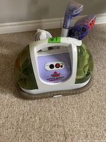 Front view of Bissell Little Green ProHeat Turbobrush cleaner with control buttons and handle visible. Unit placed on carpet.