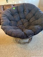 Front view of a large cushioned basket chair with plush black cushion and curved rattan frame.