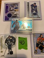 Five game-worn jersey hockey cards laid out on white surface with a green number 40 card between cards.