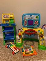 Wide view of the kids toys lot showing the Smart Shots Sports Center, toy cash register atop a blue shelving unit, colorful xylophone, and interactive kids books arranged on the floor.