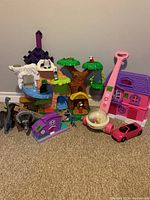 Full view of the toy lot showing playhouse, toy car, treehouse, and other toys arranged on carpet against wall