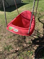 Red plastic toddler swing seat hanging outside, showing full seat and rope attachment