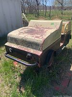 Front angled view of the metal playground car showing peeling cream paint on hood and front, black lower body with rust visible, round black headlights and metal bumper bar.