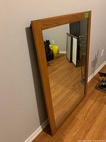 Full view of the rectangular mirror with wooden frame leaning against a wall, showing the frame color and style.