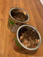 Two large metal containers filled with pennies viewed from above on a wooden floor.