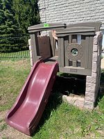 Front angle showing maroon slide, stone-effect walls, and part of the assembled playset.