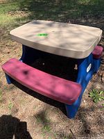 Children's plastic picnic table with tan tabletop, blue legs and maroon benches, placed outdoors showing overall condition and colors.