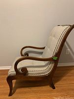 Side view showing curved wood armrest and legs of the sleigh chair with striped fabric upholstery.