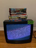 Small black CRT tube TV with static showing on screen and a stack of 11 DVDs and HD-DVDs placed on top.
