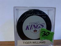 Front of the puck with Tiger Williams autograph and Los Angeles Kings logo, visible signature in silver ink with number 22.
