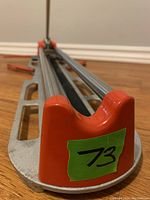 Close-up view of the tile cutter's front end showing orange cap and aluminum frame with the number 73 on a green sticker.