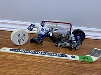 Full lot: two goalie figurines, white autographed puck, mini net, and mini hockey stick labeled Toronto Maple Leafs.