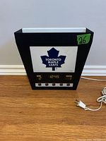 Front view of the Toronto Maple Leafs wall mount light showing logo, clock, scoreboard and electrical cord