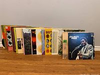 Fifteen vinyl record albums arranged standing on a wooden surface showing a variety of album covers