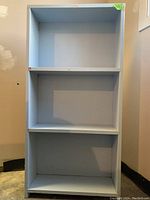 Front view of the light blue 3-shelf wood bookcase, showing overall shape and condition.