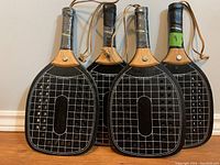 Four wooden paddleball rackets showing the front black playing surfaces with white grid and dots.